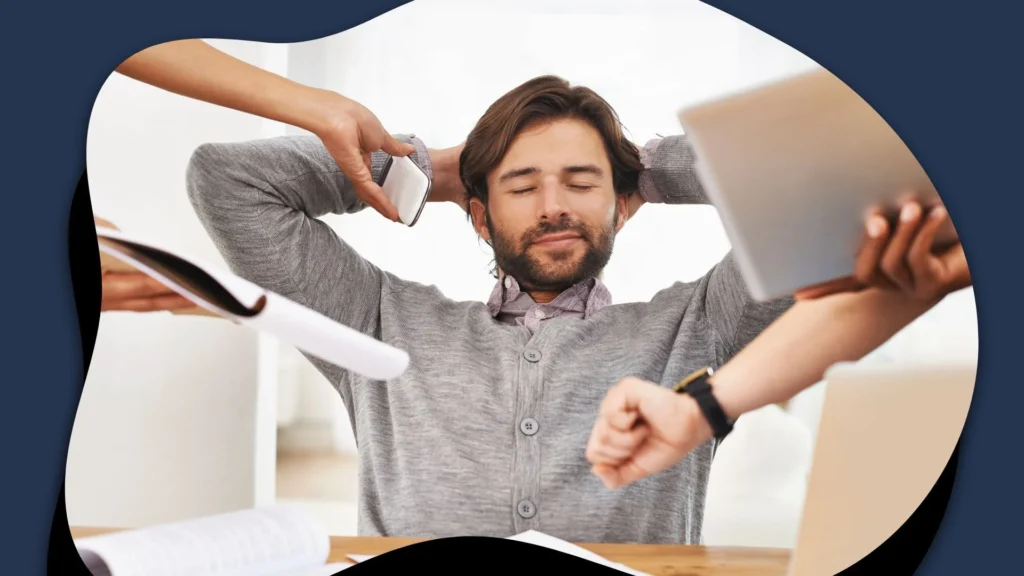 Relaxed bearded man leans back with eyes closed as coworkers present papers and a laptop, suggesting calm confidence amid workplace activity.